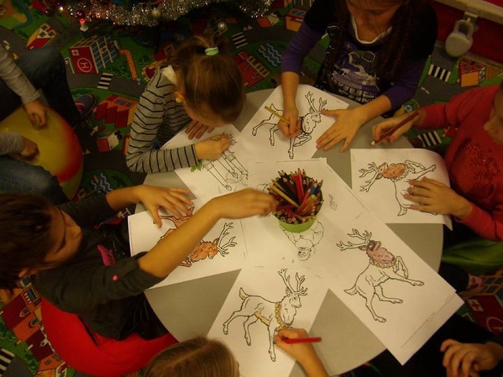 Przy stoliku siedzą dzieci wspólnie kolorują świąteczne renifery.