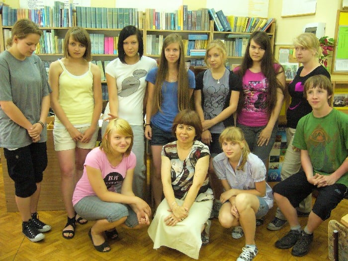 Wnętrze biblioteki, grupa dzieci z bibliotekarką Elżbietą Zakrzewską.