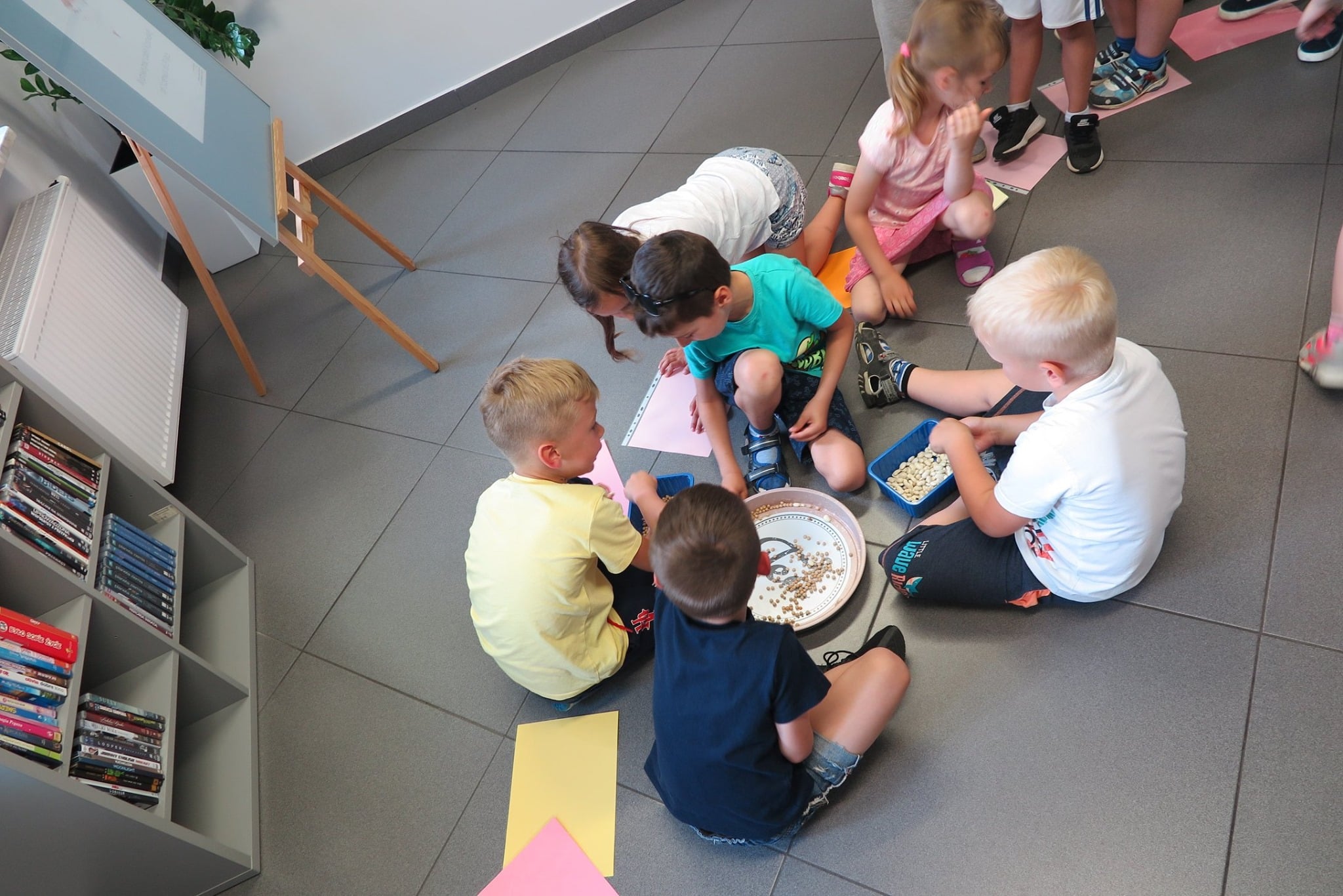 Wnętrze biblioteki, mediateka. Dzieci biorą udział w grze planszowej w ramach obchodów Dni Rodziny. Zajęcia prowadzi bibliotekarka Małgorzata Trąmpczyńska. 