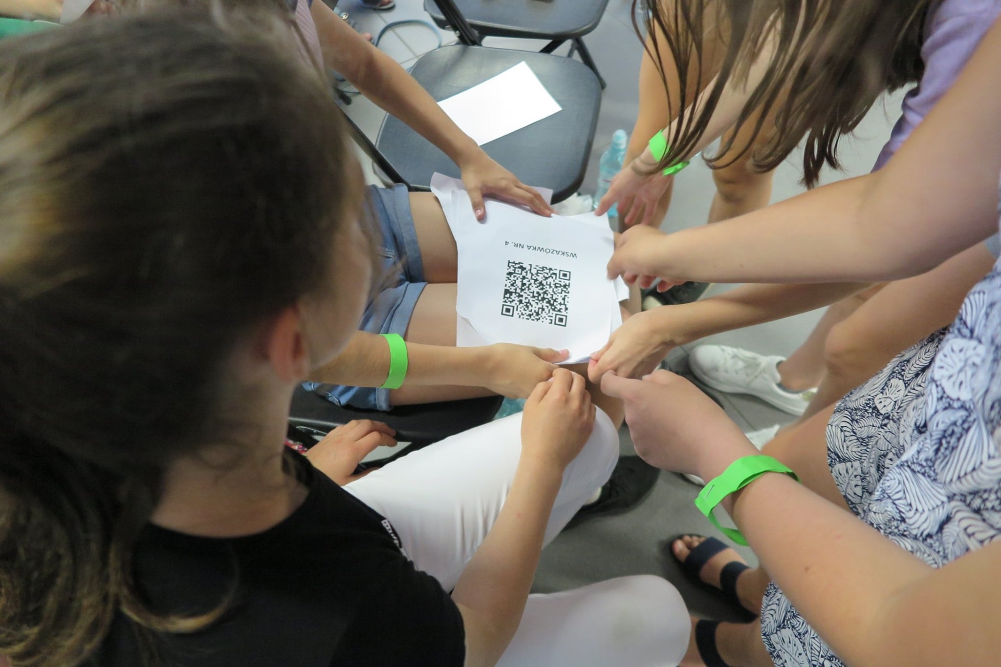 Grupa dzieci trzyma kartkę wskazówkę z kodem do gry miejskiej „Chochlikowe  psoty”.