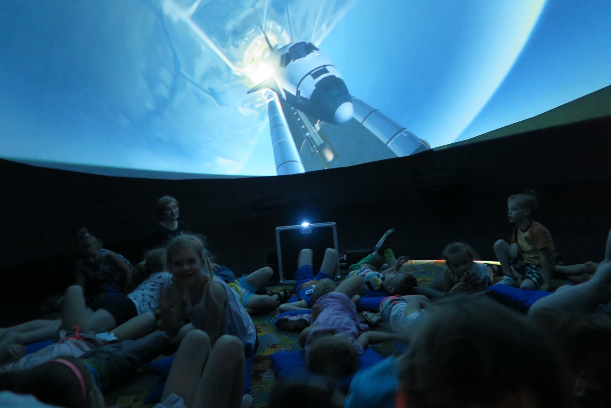 W mobilnym planetarium dzieci oglądają seans filmowy o historii lotów kosmicznych. 