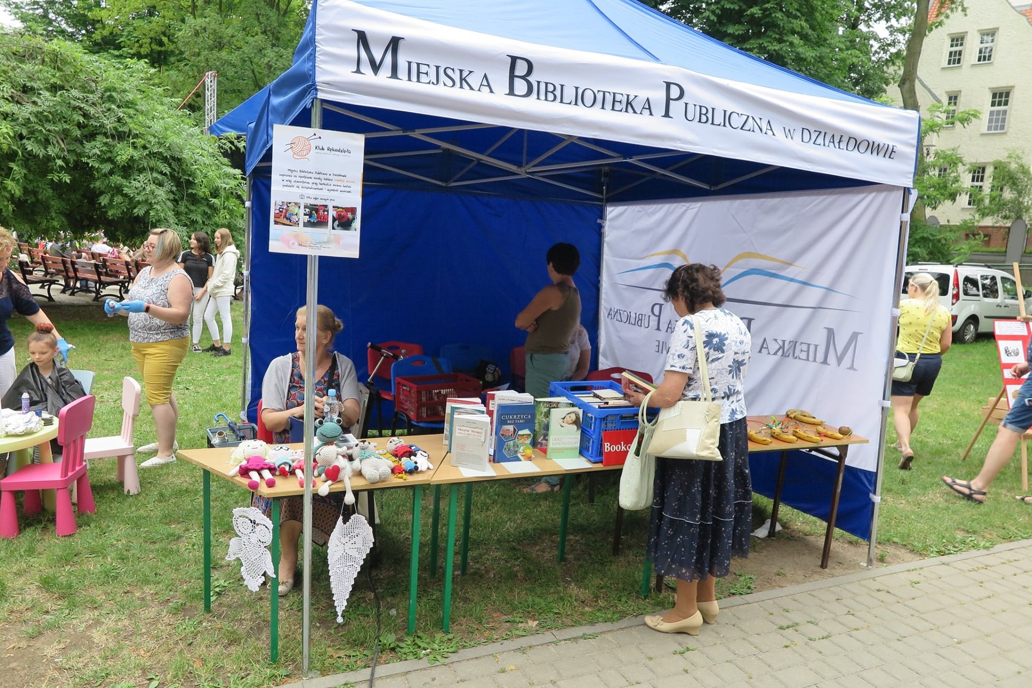 Niebieski namiot z logo MBP w Działdowie , na stoliku książki i prace wykonane przez panie z Klubu Rękodzieła.