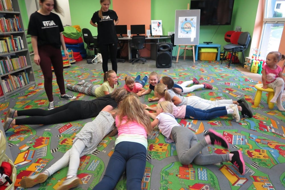Wnętrze biblioteki. Grupa dzieci biorąca udział w warsztatach tanecznych. 