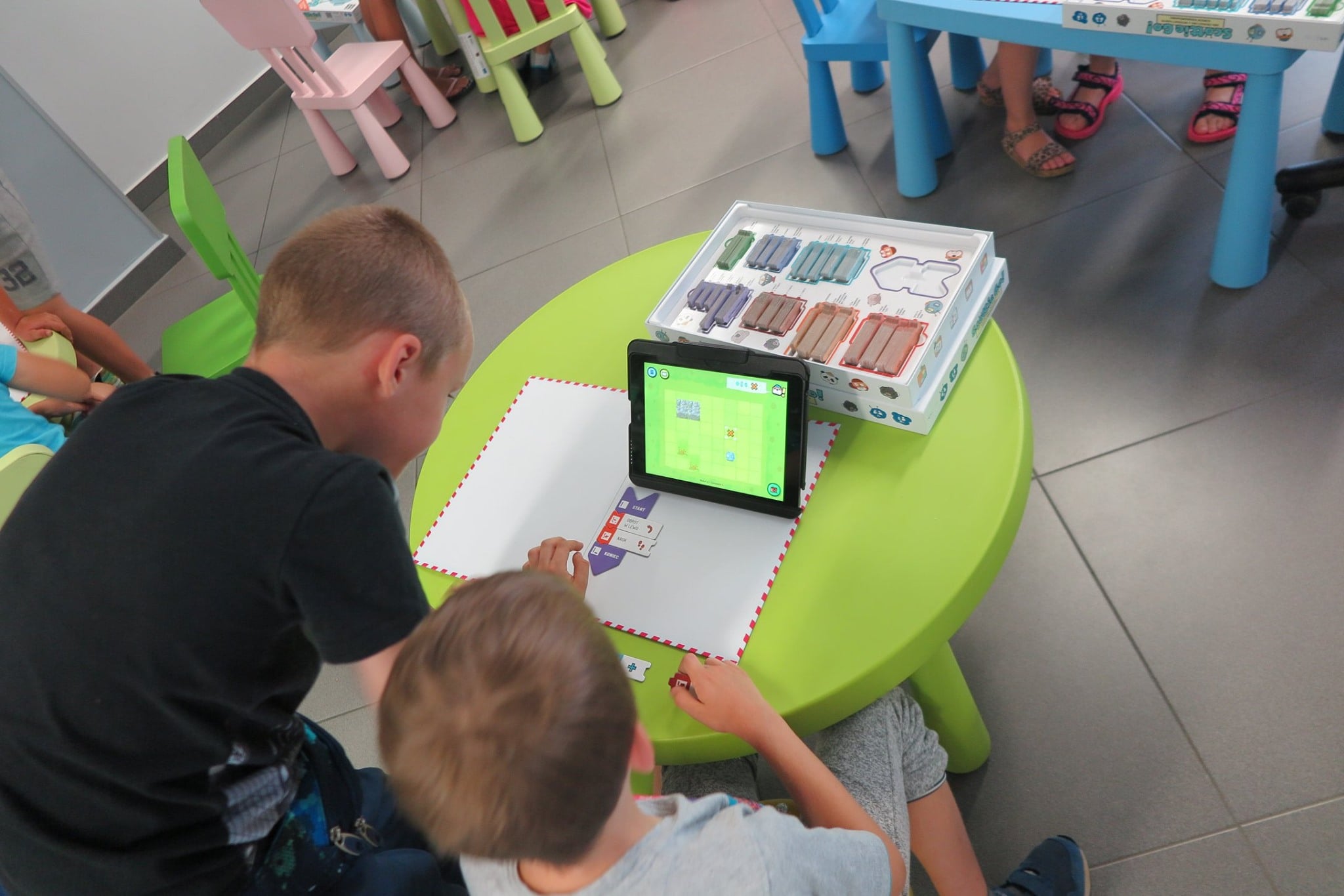 Na stoliku gra z programowania ''Scottie Go'' i tablet na którym gra dwóch chłopców.