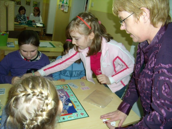 Przy stoliku grupa dzieci gra w monopol obok bibliotekarka Marzena Pawłowska.