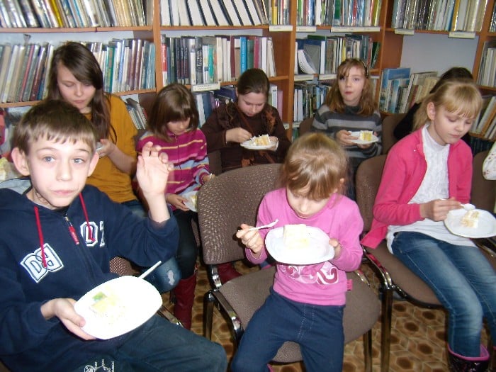 Grupa dzieci je tort z okazji zakończenia ferii w bibliotece.