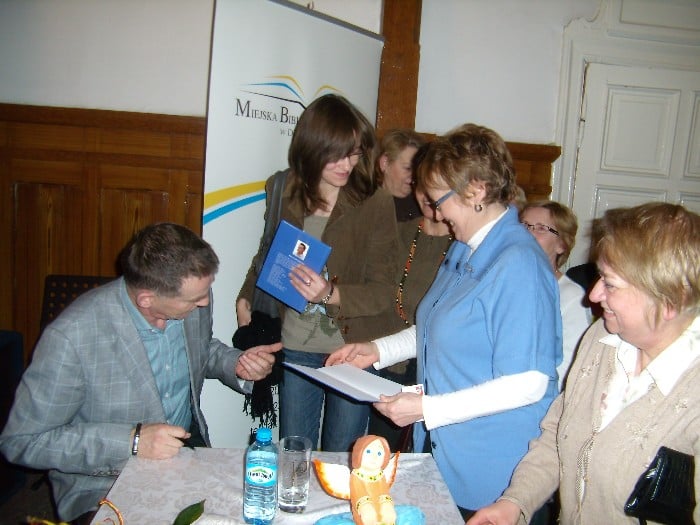 Przy stoliku siedzi autor Krzysztof Tabaczka i podpisuje czytelnikom książki.