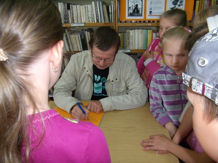 Wnętrze biblioteki, grupa dzieci biorąca udział w spotkaniu  z Andrzejem Markiem Grabowskim.