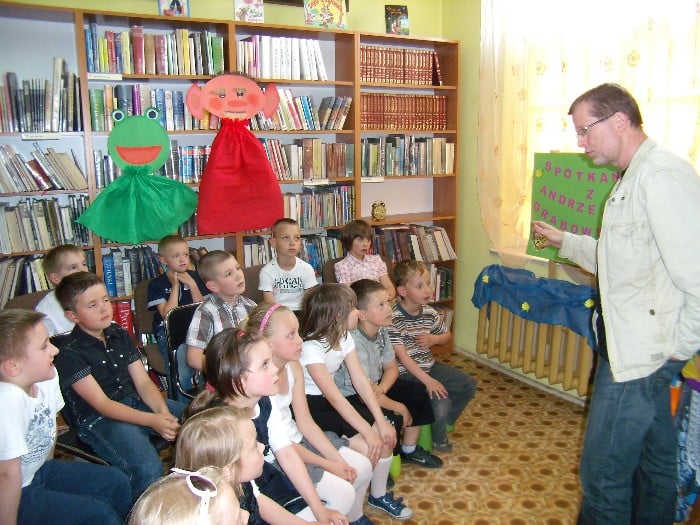 Wnętrze biblioteki, grupa dzieci biorąca udział w spotkaniu  z Andrzejem Markiem Grabowskim.