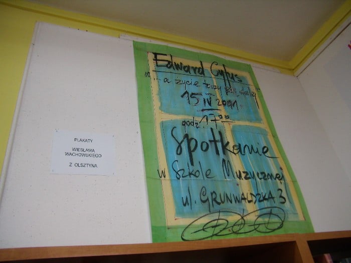 Wnętrze biblioteki, na ścianie wiszą plakaty Wiesława Wachowskiego.