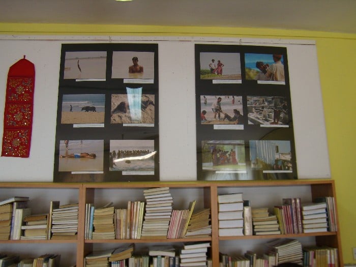Wnętrze biblioteki, nad regałem z książkami wiszą zdjęcia wykonane przez Joannę Gorczyce. 