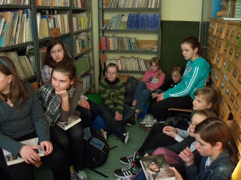 Wnętrze biblioteki. Grupa dzieci z DKK SP 3 wspólnie omawia  książkę Anny Mieszkowskiej "Dzieci Ireny Sendlerowej".