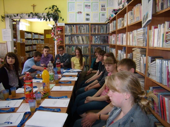Wnętrze biblioteki, przy stole siedzi młodzież zgromadzona na warsztaty dziennikarskie z Markiem Barańskim redaktorem Gazety Olsztyńskiej.