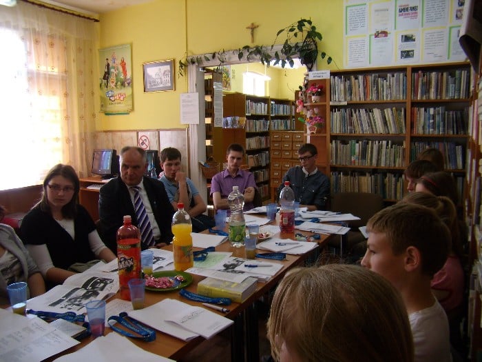Wnętrze biblioteki, przy stole siedzi młodzież zgromadzona na warsztaty dziennikarskie z Markiem Barańskim redaktorem Gazety Olsztyńskiej.