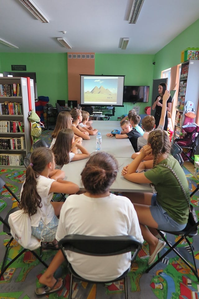 Wnętrze biblioteki, oddział dla dzieci. Warsztaty archeologiczne prowadzi z dziećmi Anna Jaklewicz. W tle na ekranie piramidy.