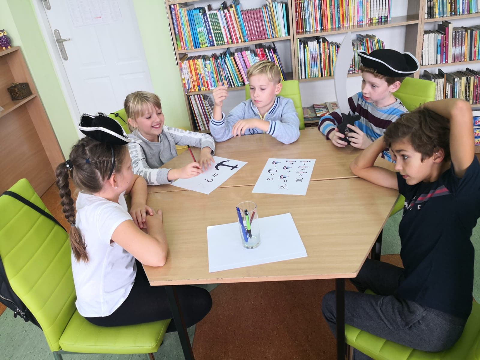 Wnętrze biblioteki, pięcioro dzieci siedzi przy stoliku i rozwiązuje zagadki pirackie.