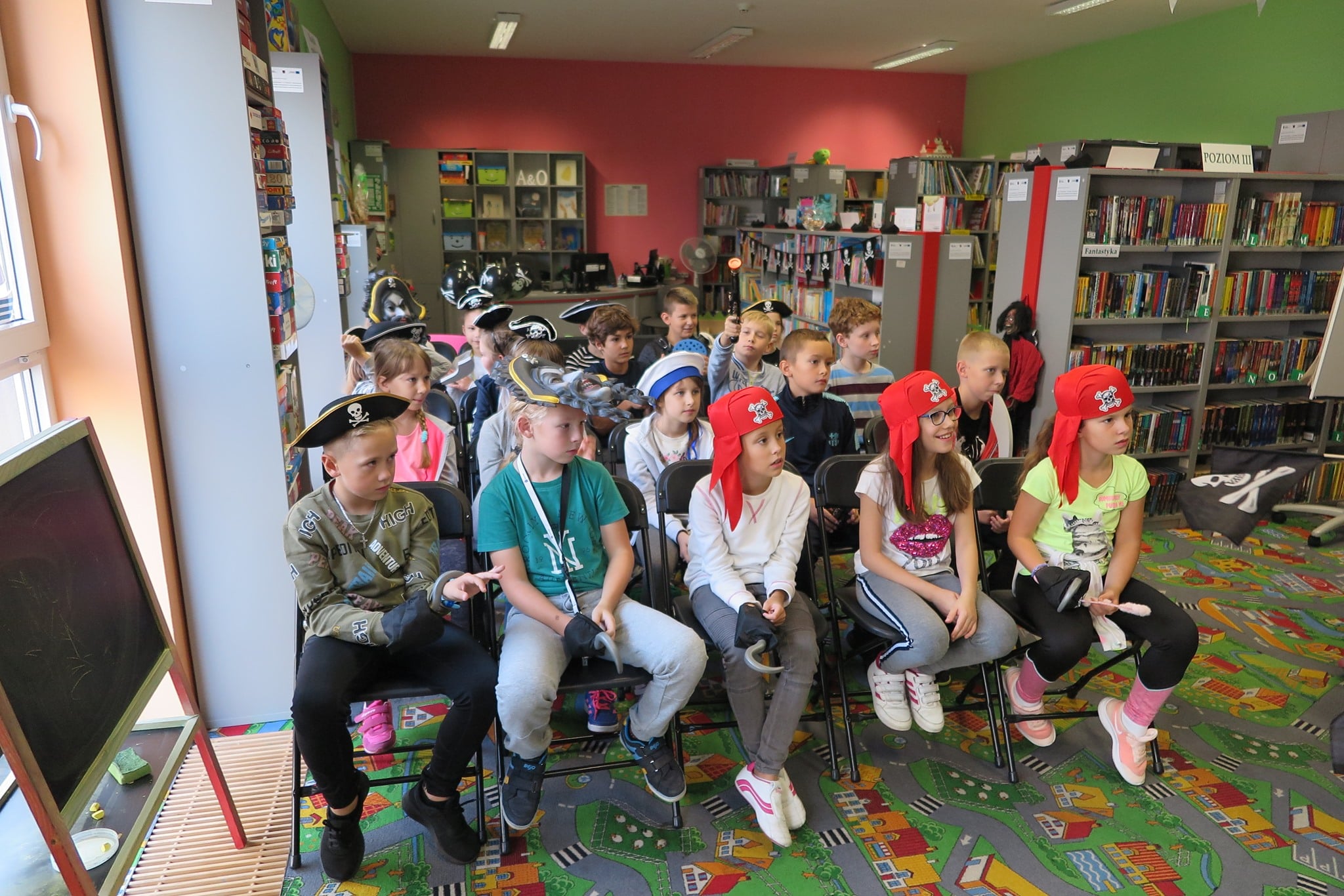 Wnętrze biblioteki, grupa dzieci siedzi na krzesełkach w pirackich strojach.