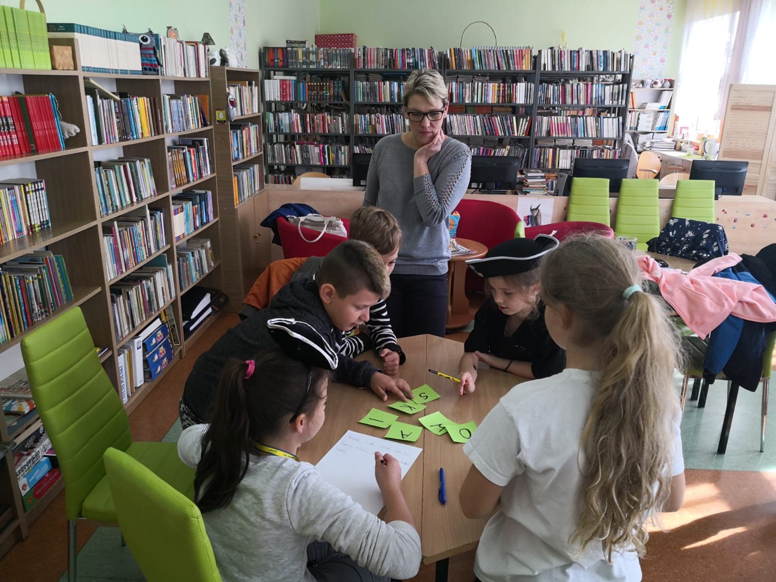 Wnętrze biblioteki, pięcioro dzieci siedzi przy stoliku i rozwiązuje zagadki pirackie.