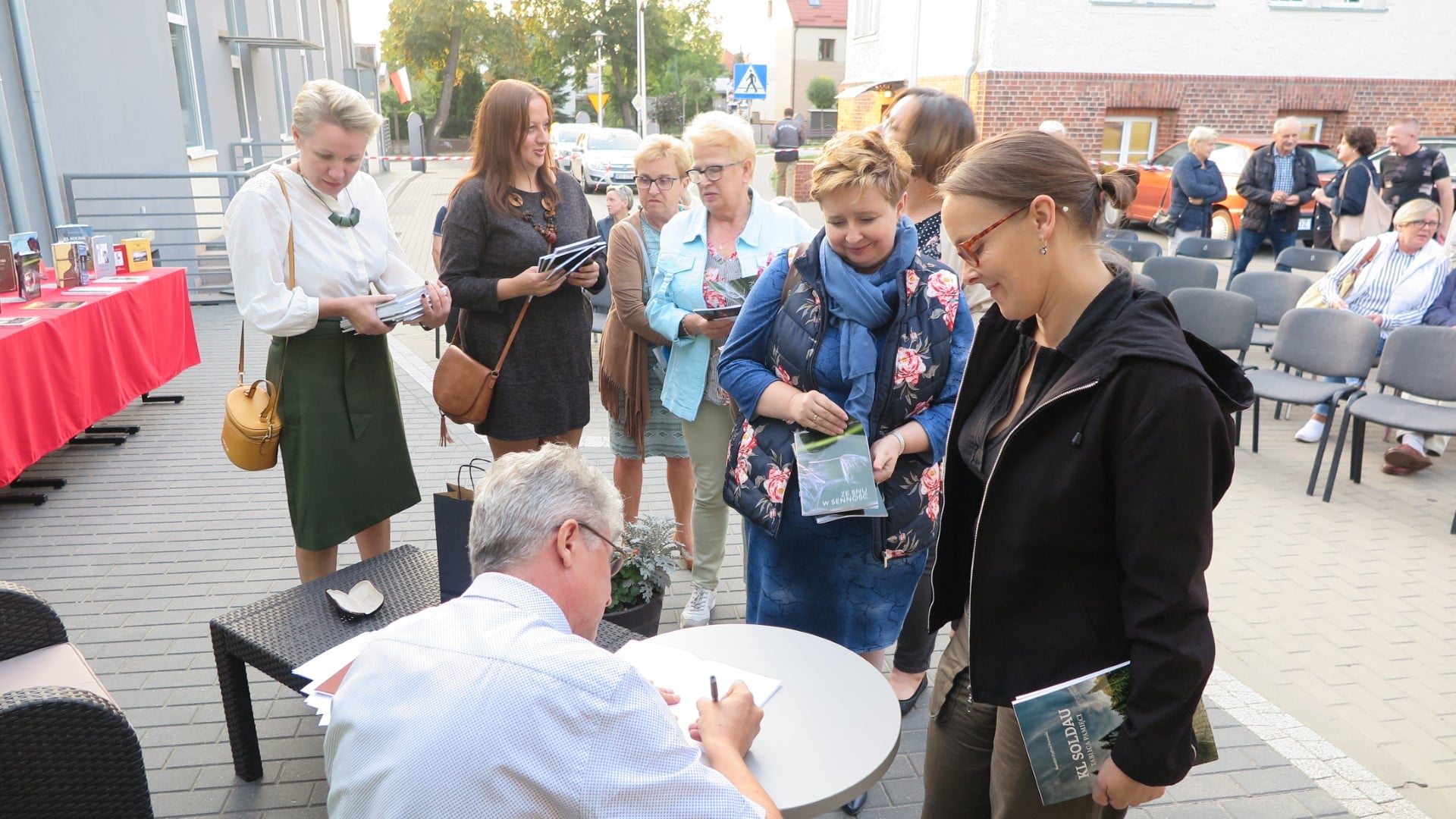 Na placu przed MBP w Działdowie, przy stoliku siedzi Benedykt Zygfryd Perzyński autor tomiku poezji i podpisuje swoją książkę.