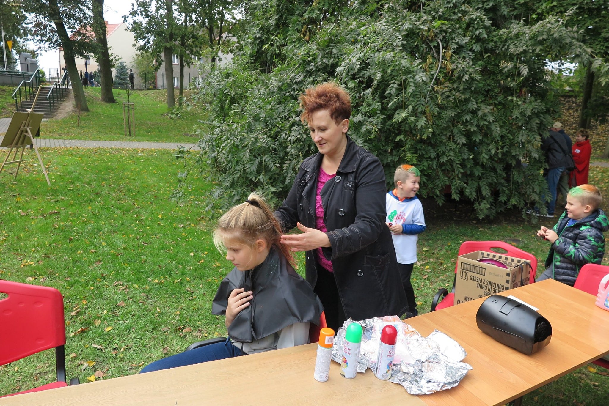 W parku na stoliku spraye do włosów. Dorota Leśniewska układa włosy młodej dziewczynce.