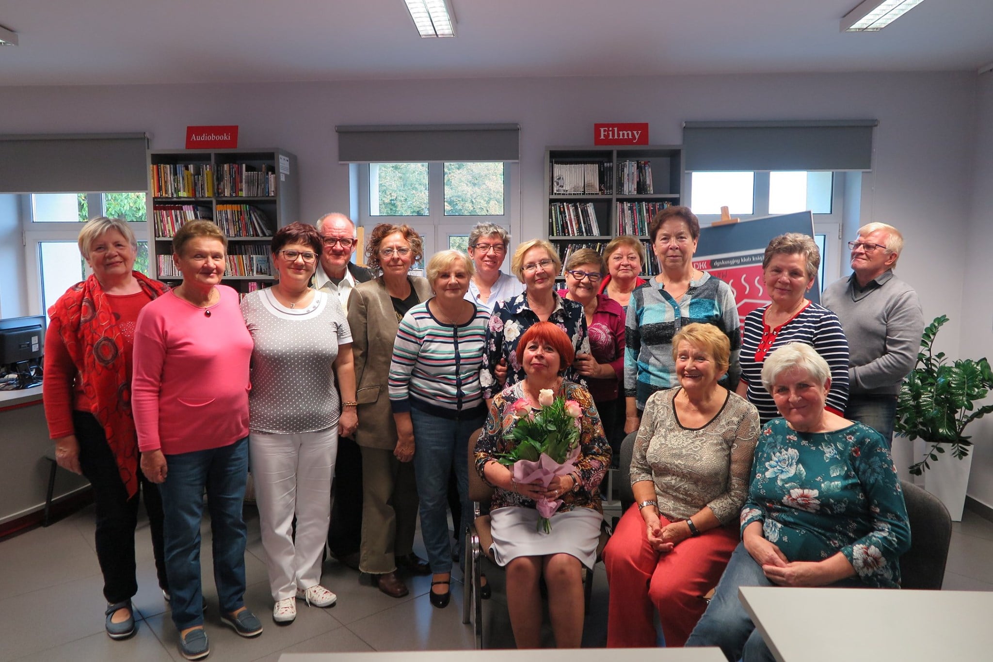 Wnętrze biblioteki,mediateka. Członkowie klubu DKK UTW na czele z autorką omawianej książki Elżbietą Zakrzewską. 