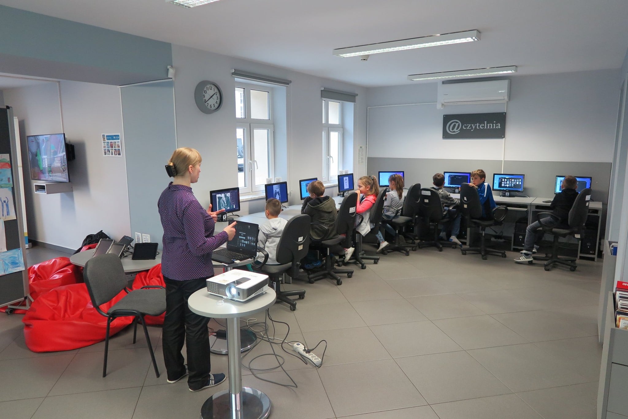 Bibliotekarka Małgorzata Trąmpczyńska prowadzi warsztaty w ramach projektu ,,Wielkie kopiowanie mistrza Skurpskiego''.  Dzieci siedzą przy komputerach i robią wirtualne plakaty. 