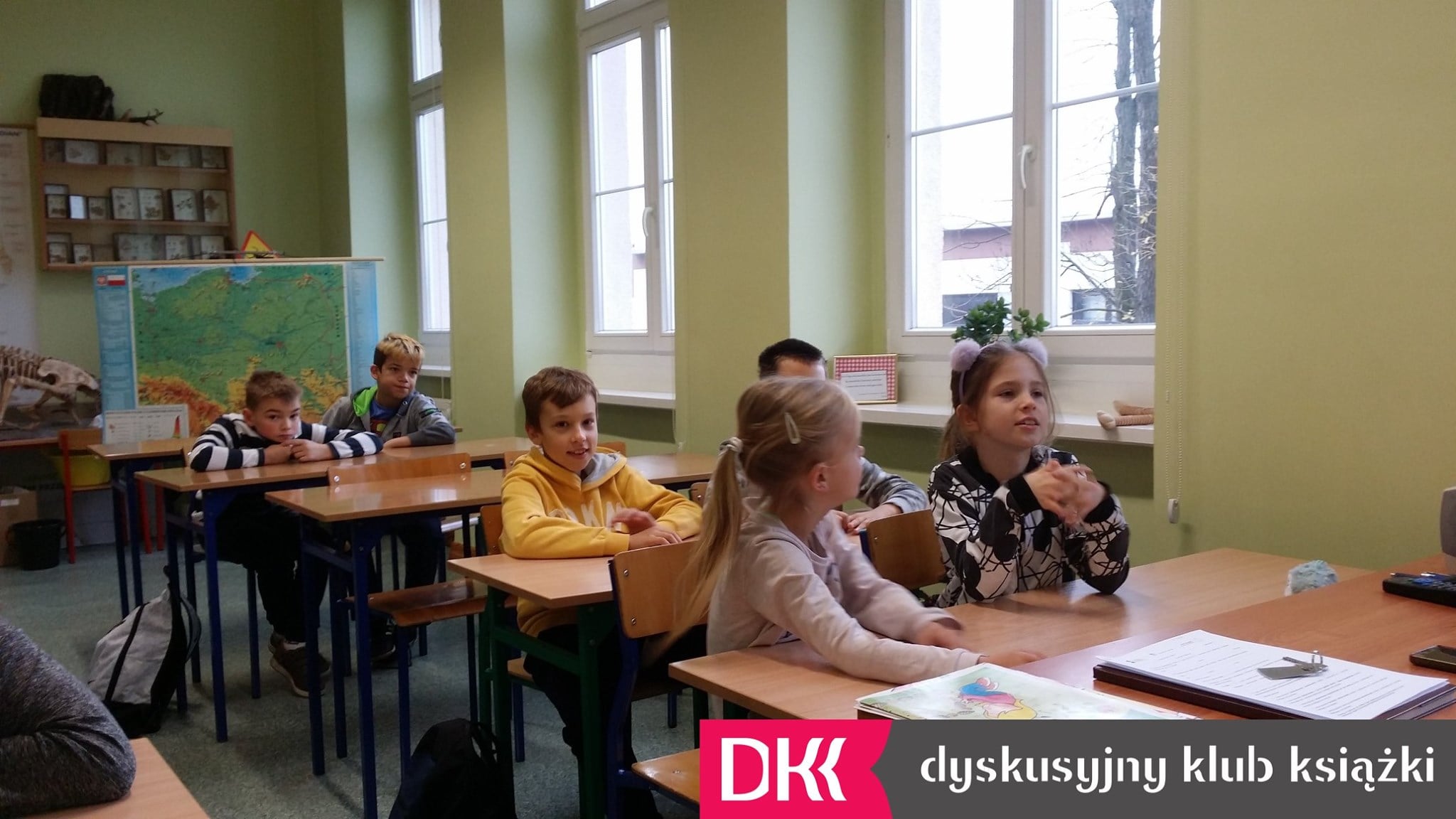 Wnętrze klasy dzieci siedzą w ławkach. Spotkanie DKK ,omawiana książka ''Asiunia'' Joanny Papuzińskiej.