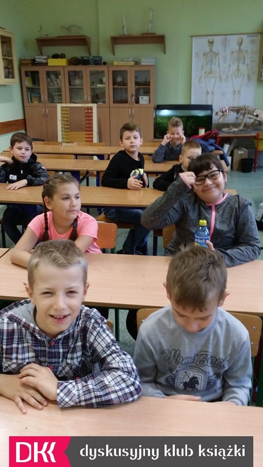 Wnętrze klasy dzieci siedzą w ławkach. Spotkanie DKK ,omawiana książka ''Asiunia'' Joanny Papuzińskiej.