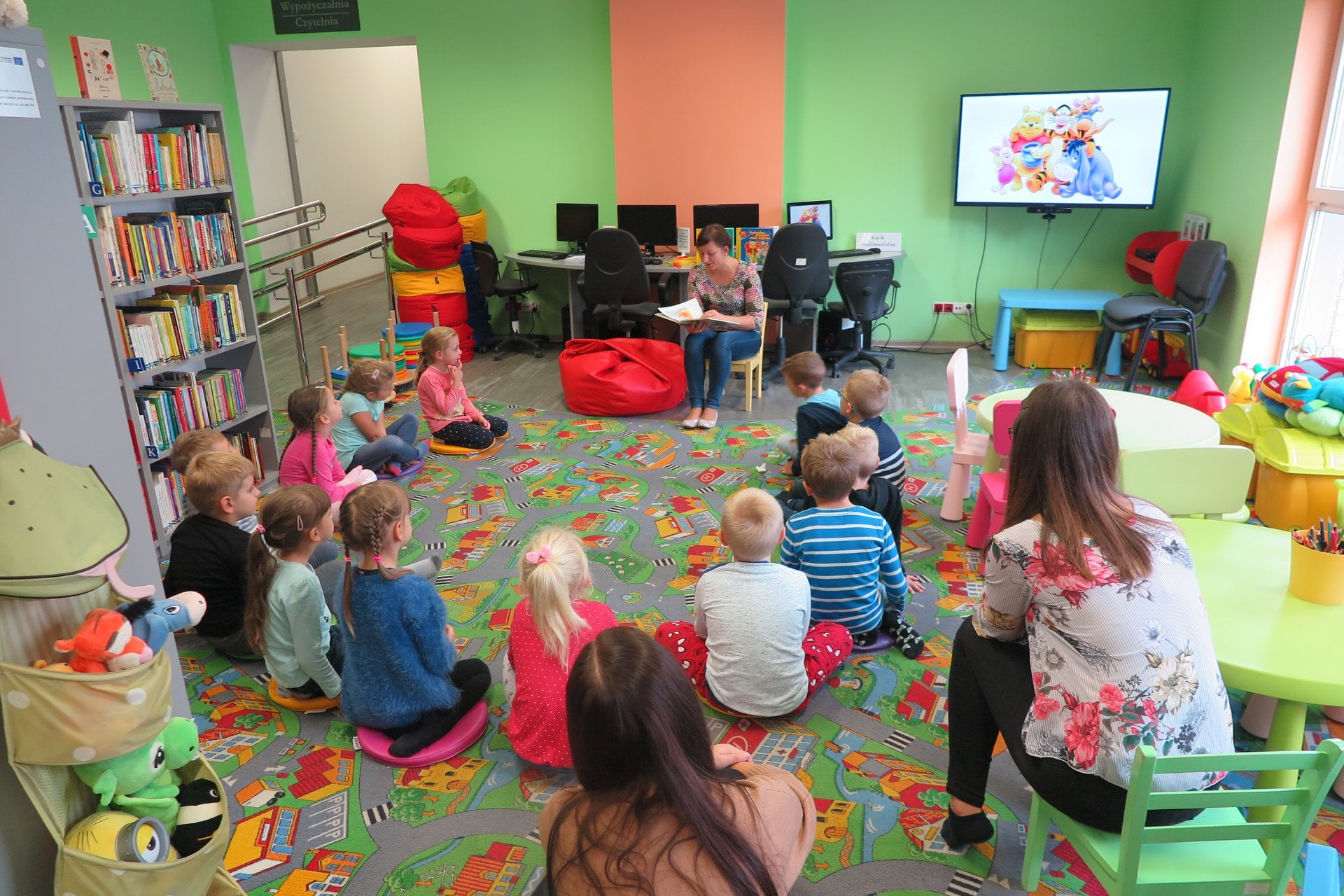 W oddziale dla dzieci siedzą w kole przedszkolaki grupa ''Pszczółki'', słuchają opowiadania o Kubusiu Puchatku. Zajęcia prowadzi bibliotekarka Ania Wiśniewska.