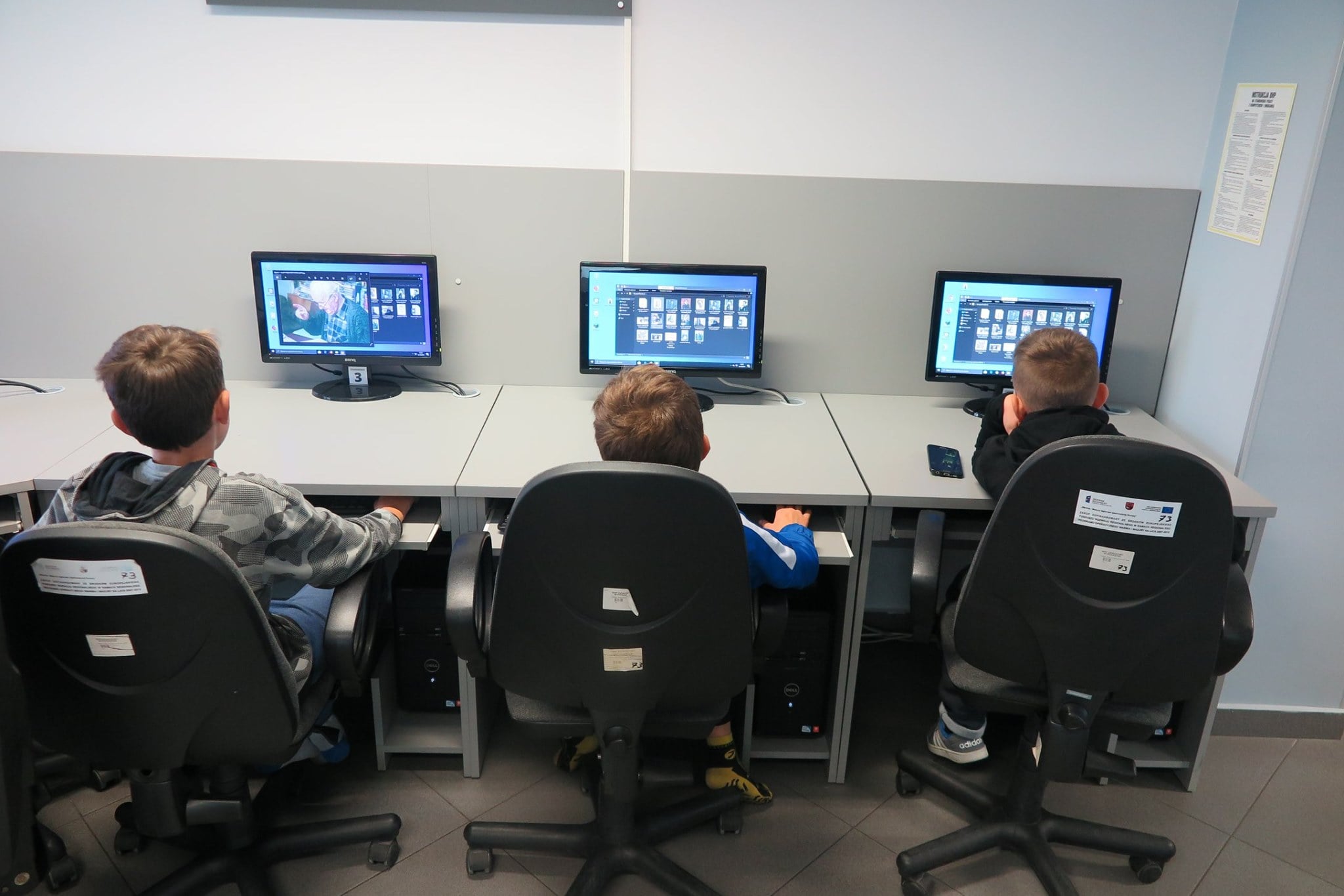 Wnętrze biblioteki,mediateka. Trzech młodych uczestników projektu siedzi przy komputerach i tworzą wirtualne plakaty dotyczące życia i twórczości Hieronima Skurpskiego. 