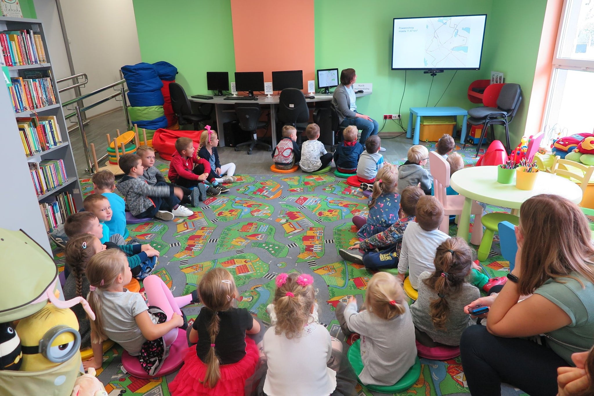 Wnętrze biblioteki, oddział dla dzieci. Na pufach siedzą przedszkolaki z grupy ''Jeżyki'' z Przedszkola nr 1. Zajęcia prowadzi bibliotekarka Ania Wiśniewska .