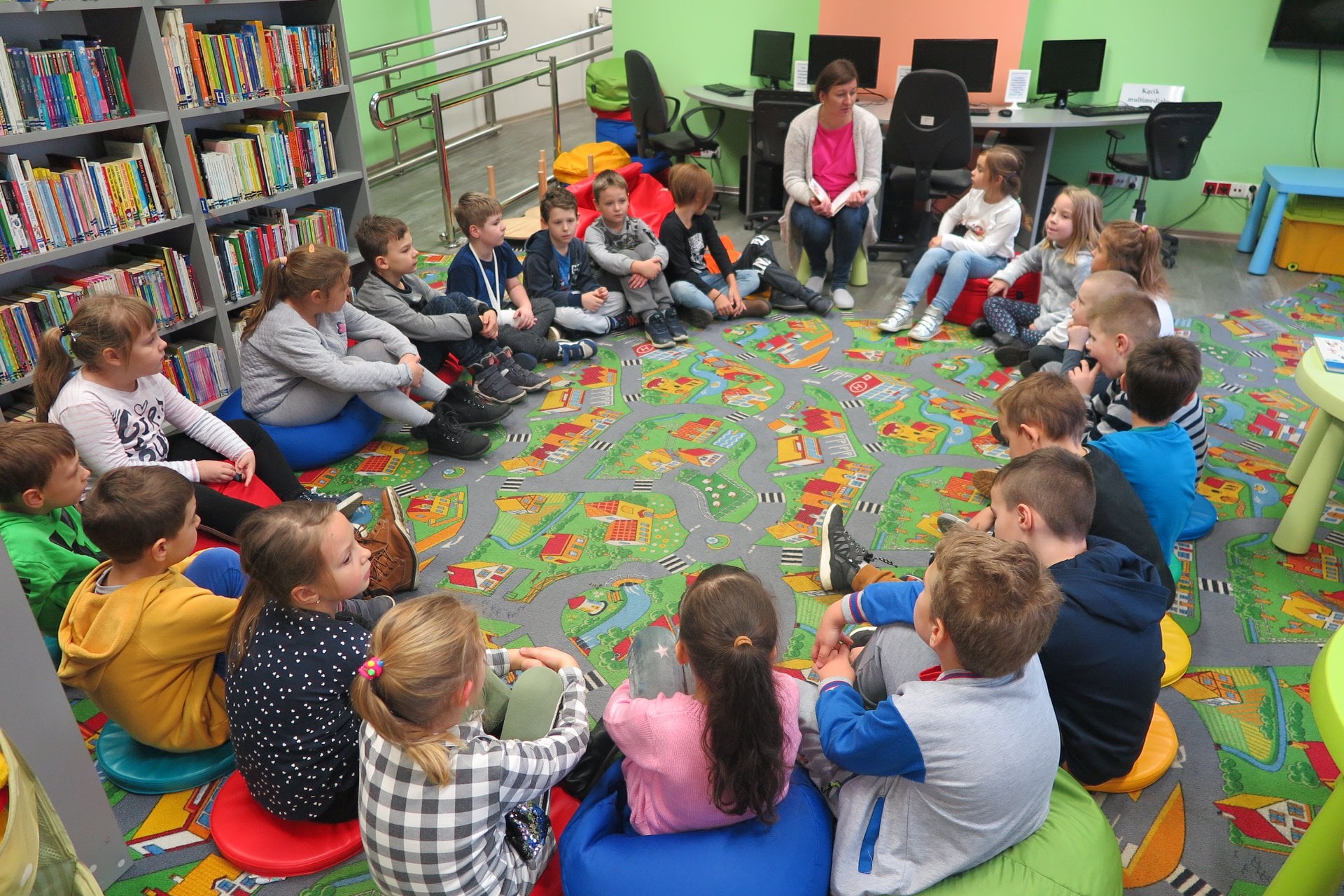 Wnętrze biblioteki. Dzieci z klasy Ib ze SP nr 2 w Działdowie siedzą w kole. Zajęcia prowadzi bibliotekarka Ania Wiśniewska. 