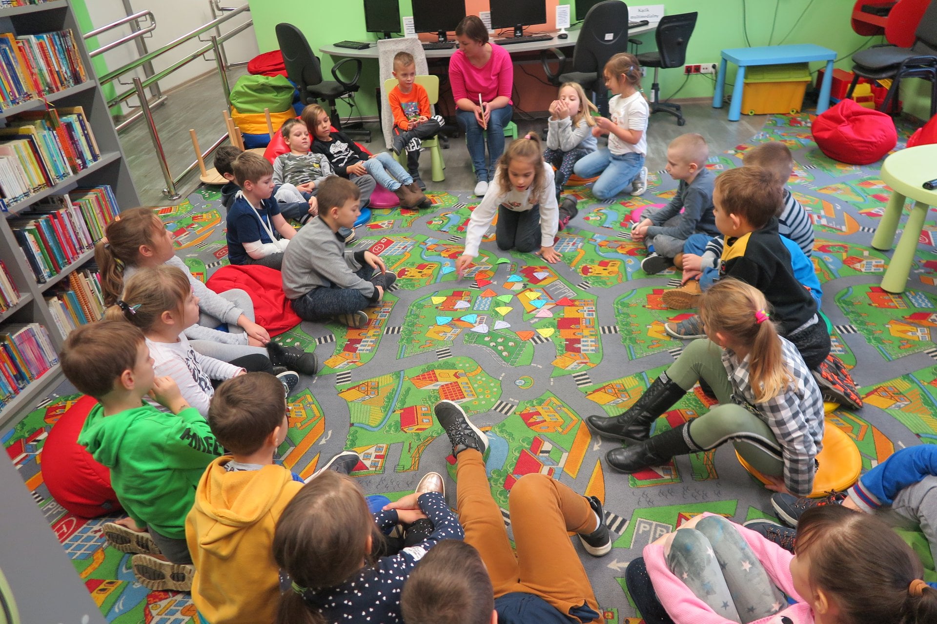 Wnętrze biblioteki. Dzieci z klasy Ib ze SP nr 2 w Działdowie siedzą w kole. Zajęcia prowadzi bibliotekarka Ania Wiśniewska. 