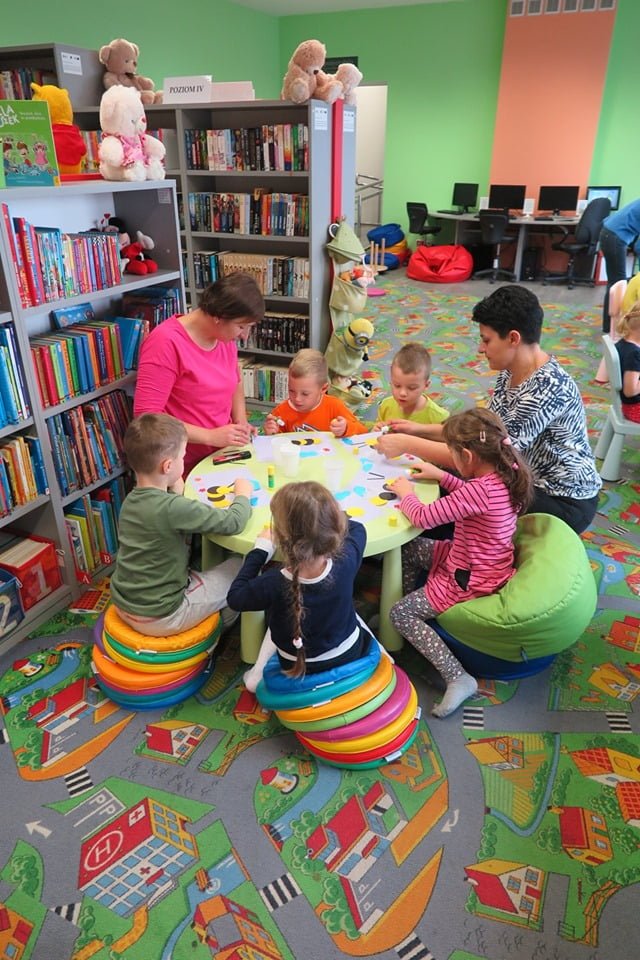Wnętrze biblioteki. dzieci z grupy III z Przedszkola nr 4 siedzą  na kolorowych pufach i wykonują pszczółki z wcześniej przygotowanych elementów.