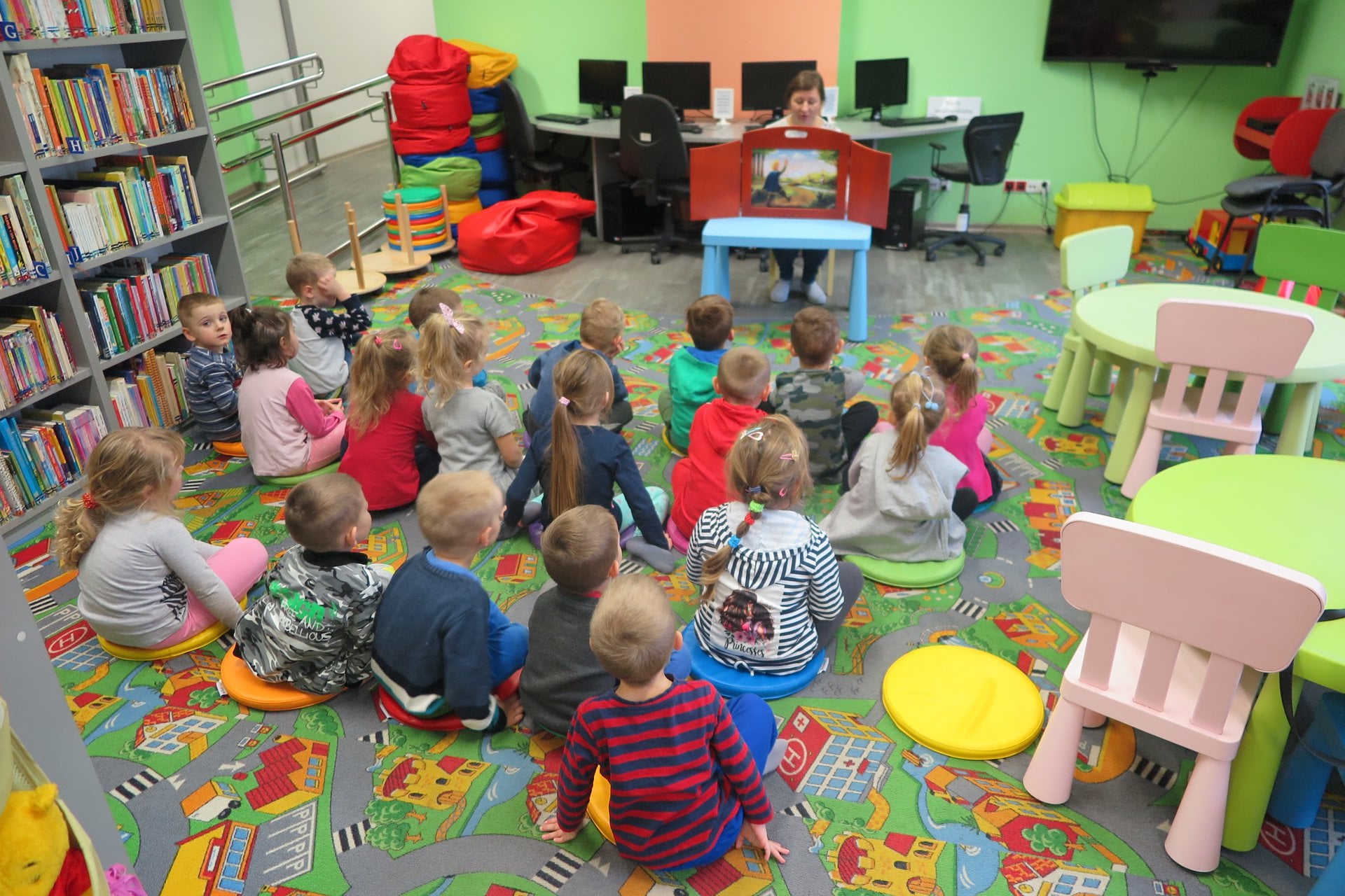 Wnętrze biblioteki. Dzieci z przedszkola nr 3 słuchają teatrzyku kamishibai ''Królowa pszczół''. Zajęcia prowadzi bibliotekarka Ania Wiśniewska.