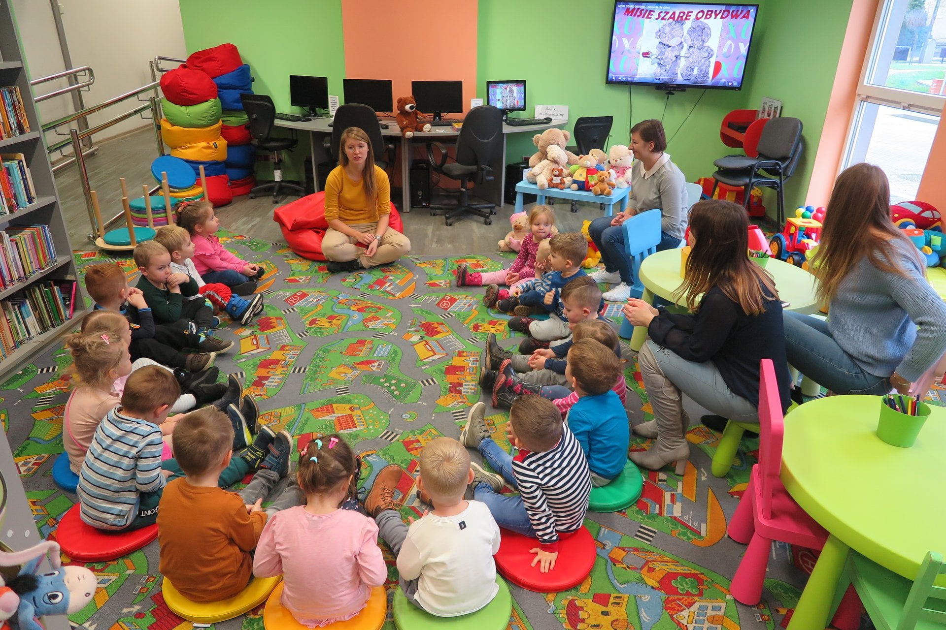 Wnętrze biblioteki. Dzieci z przedszkola ''U Misia'' siedzą w okręgu i słuchają opowiadania o misiach. Zajęcia prowadzi bibliotekarka Aleksandra Cybulska. 