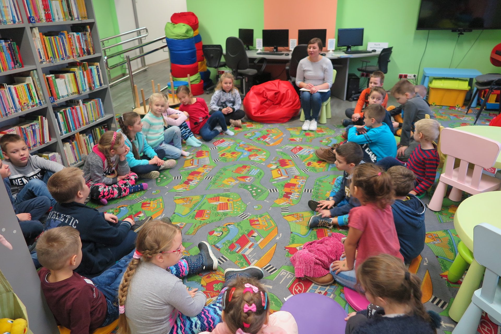 Wnętrze biblioteki. Dzieci z klasy Ic ze Szkoły Podstawowej nr 2 siedzą w kole i biorą udział w zajęciach na temat wartości. Bibliotekarka Ania Wiśniewska prowadzi zajęcia. 