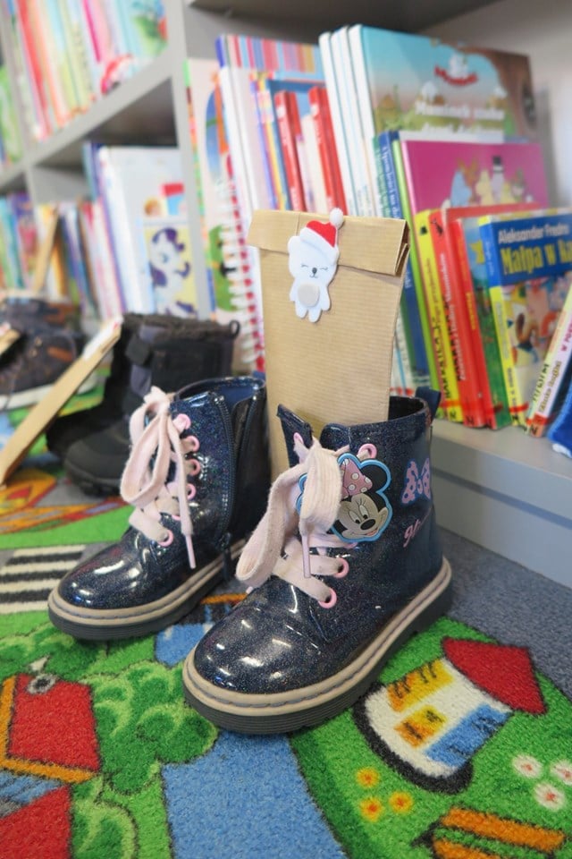Wnętrze biblioteki. Na dywanie buty dzieci a w nich małe upominki z okazji mikołajek.