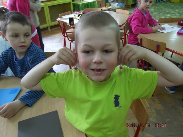 Chłopiec trzyma przy uszach kolczyki wykonane na warsztatach jubilerskich.