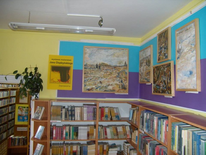 Wnętrze biblioteki, na ścianie wisi wystawa malarstwa Jana Chądzyńskiego z Mławy.