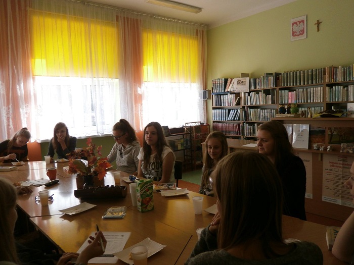 Wnętrze biblioteki, przy stolikach siedzą członkowie DKK GIM NR 2 omawiają książkę A. Olejnik "Zabłądziłam".