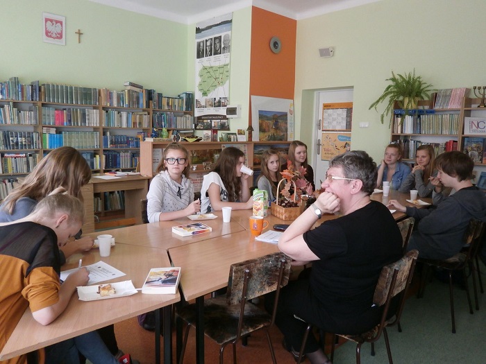 Wnętrze biblioteki, przy stolikach siedzą członkowie DKK GIM NR 2  z panią Ewą Sotomską omawiają książkę A. Olejnik "Zabłądziłam".