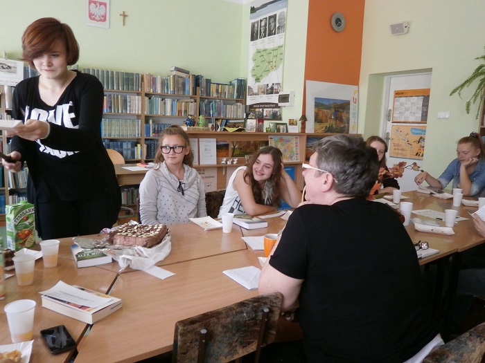 Wnętrze biblioteki, przy stolikach siedzą członkowie DKK GIM NR 2  z panią Ewą Sotomską omawiają książkę A. Olejnik "Zabłądziłam".
