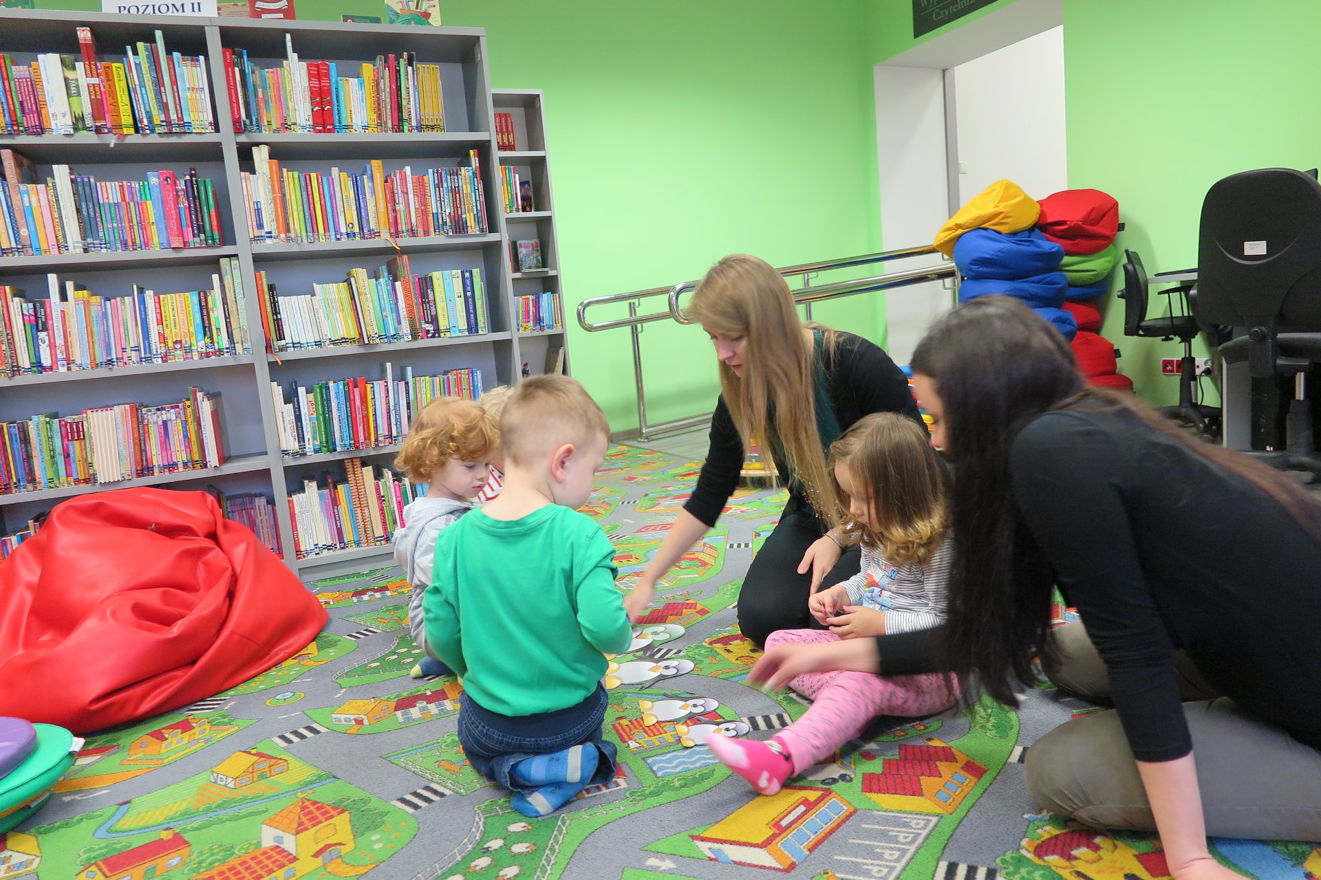 Wnętrze biblioteki (Klub Malucha) bibliotekarka Aleksandra Cybulska prowadzi zajęcia z dziećmi.