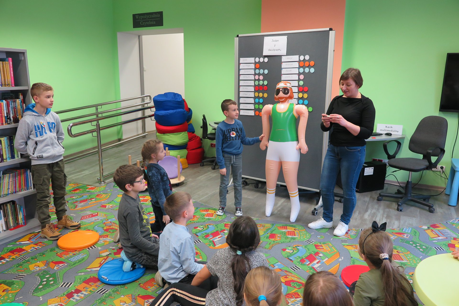 Wnętrze biblioteki, z okazji ferii grupa dzieci bierze udział w ''Fabryce Zimowych Pomysłów w MBP''. Zajęcia prowadzi bibliotekarka Ania Wiśniewska. 