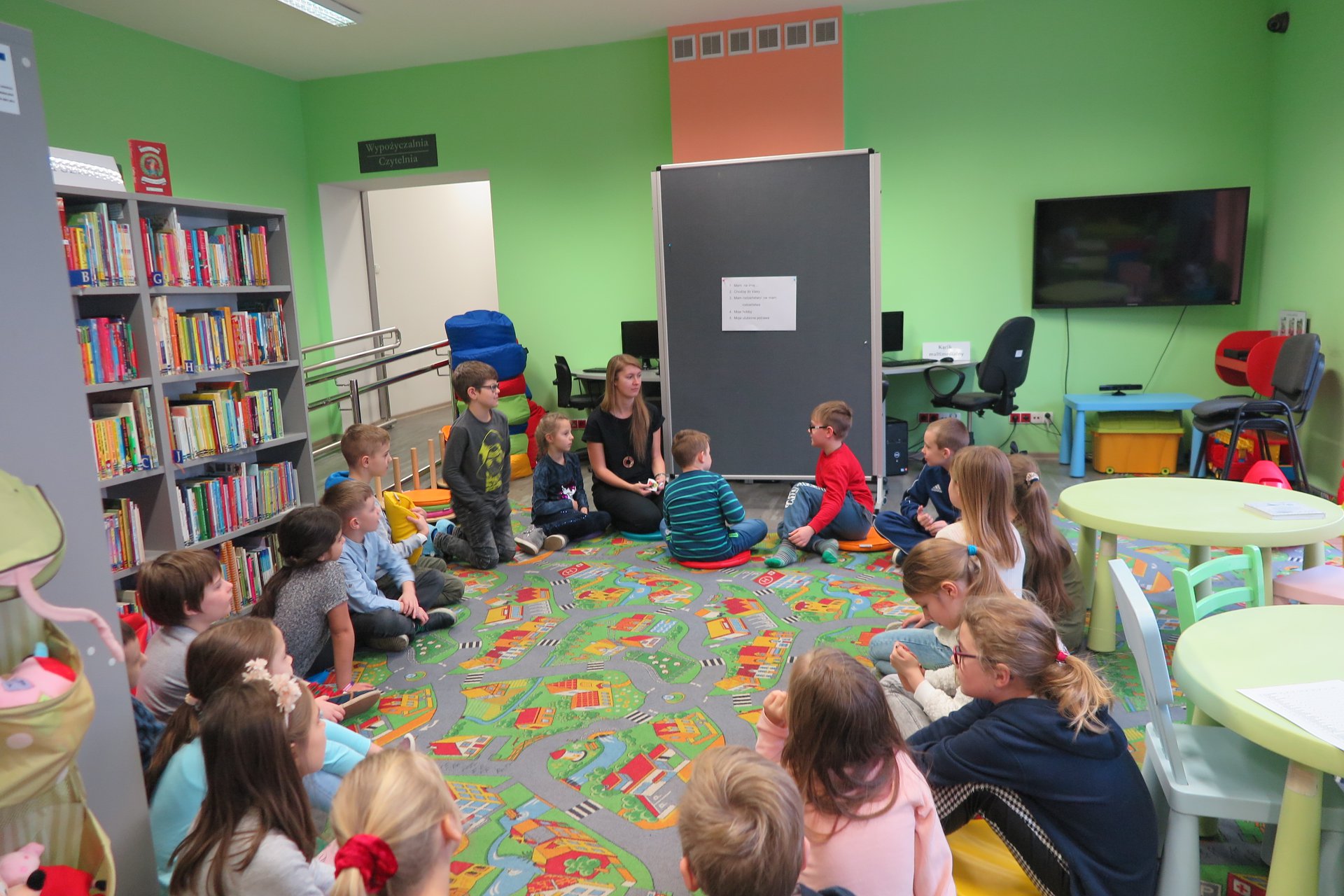 Wnętrze biblioteki, z okazji ferii grupa dzieci bierze udział w ''Fabryce Zimowych Pomysłów w MBP''. Zajęcia prowadzi bibliotekarka Aleksandra Cybulska. 