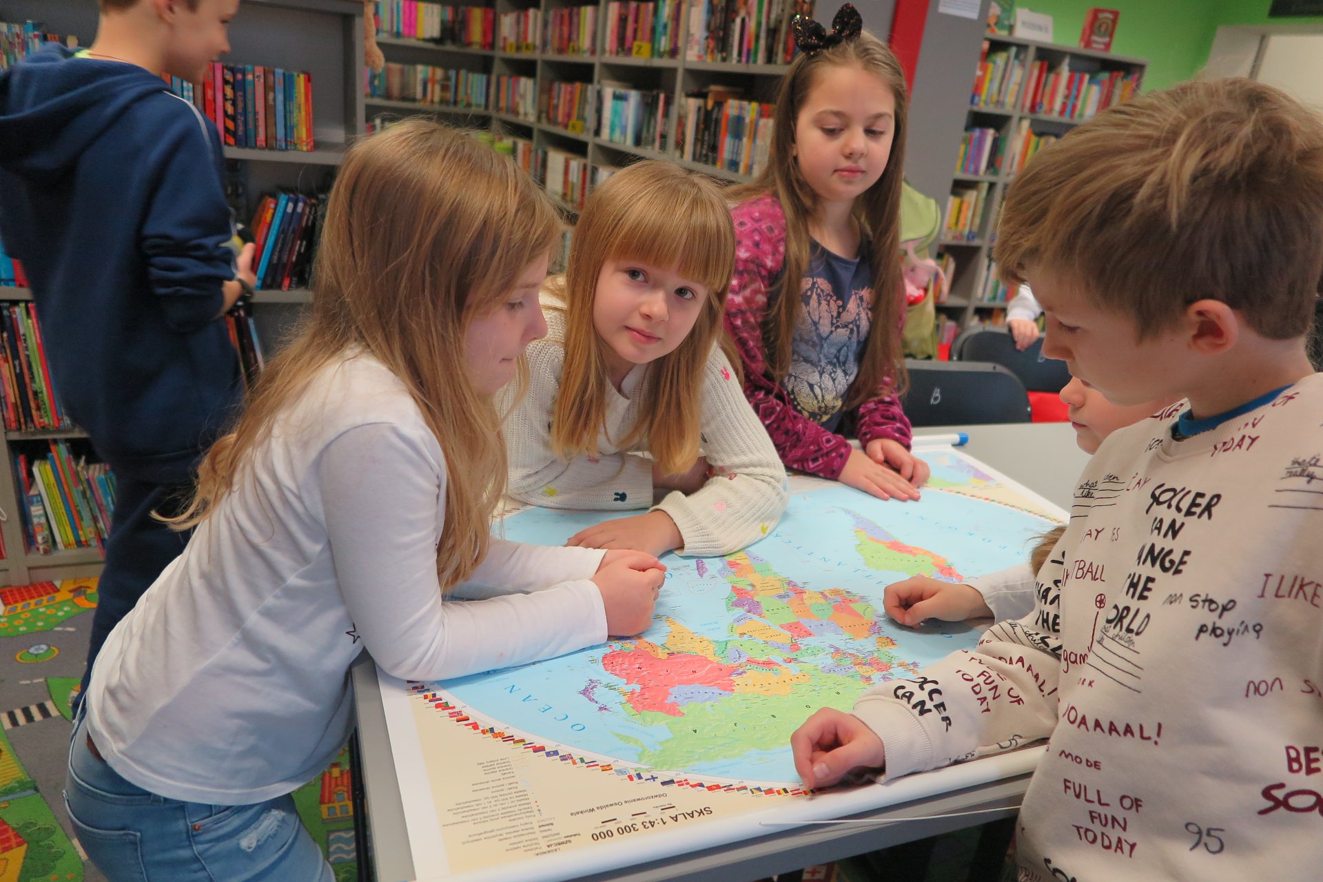 Wnętrze biblioteki (Klub Malucha) warsztaty geograficzne, czworo dzieci ogląda mapę świata.
