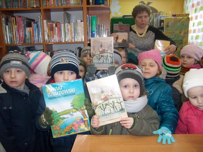 Wnętrze biblioteki, grupa dzieci wypożycza książki o Działdowie.