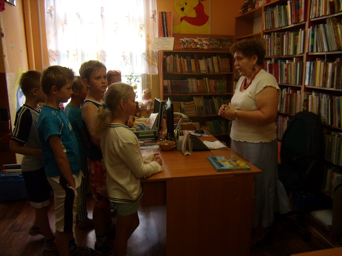Grupa dzieci w bibliotece podczas lekcji bibliotecznej poznają układ książek na półkach i zasady wypożyczania.