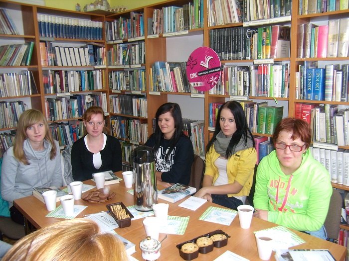 Wnętrze biblioteki. Przy stoliku siedzą członkinie DKK ZS Malinowo wspólnie omawiają książkę  R.P. Evansa "Papierowe marzenia".